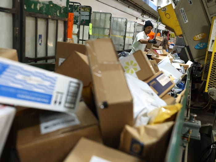 A worker pulls packages from a bin onto a conveyor belt at distribution facility