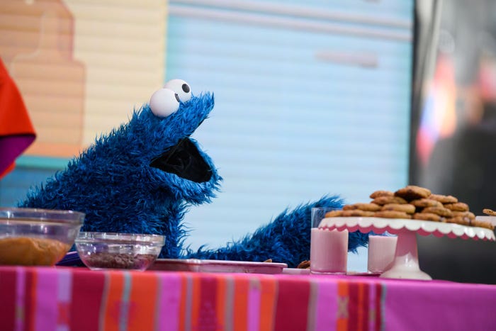 Cookie Monster reaching toward a plate of cookies.