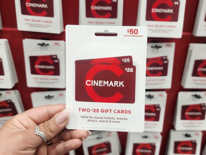 A hand holds a red Cinemark gift card in front of a wall of red Cinemark gift cards at Costco