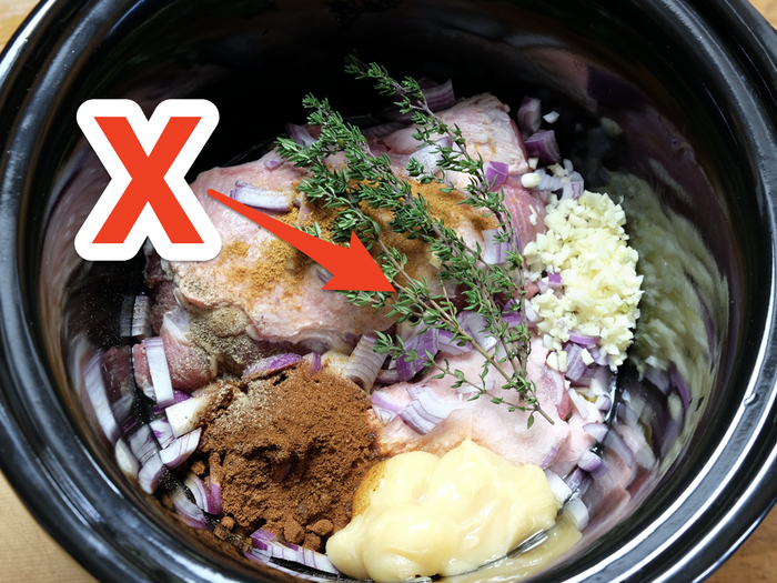 red arrow pointing at meat cooking in the slow cooker with spices, herbs, and flavorings