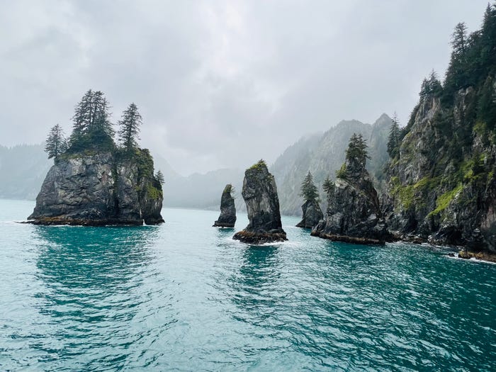 Large rock formations with trees jet out of blue waters on a cloudy day.