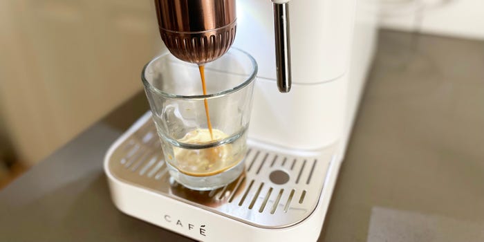 A close up shot of the GE Cafe Affetto brewing a shot of espresso into a glass demitasse.