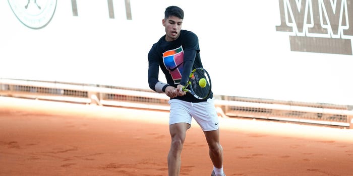 Carlos Alcaraz of Spain practices on clay courts during the Mutua Madrid Open 2024. He swings his racket against a ball.