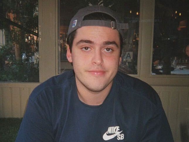 Alex sitting at a restaurant table wearing a blue Nike shirt and backwards hat, smiling.