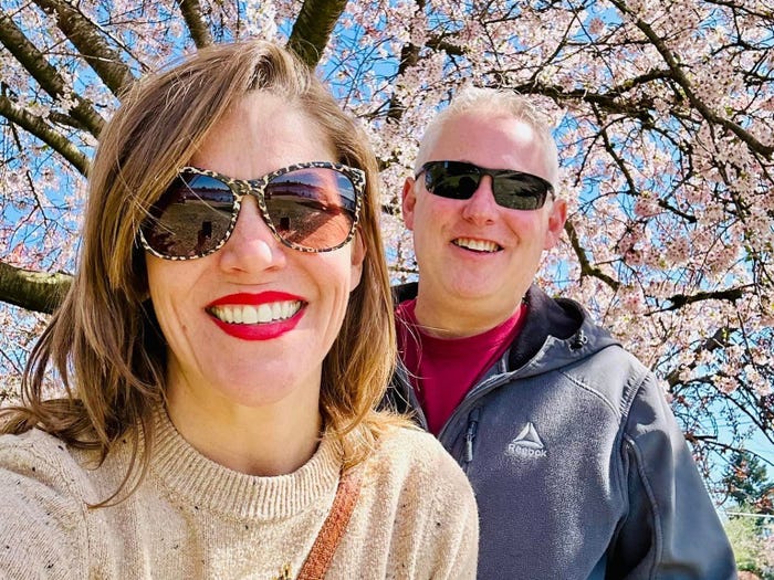 Woman and man wearing sunglasses and standing on a pink cherry blossom tree in Seattle