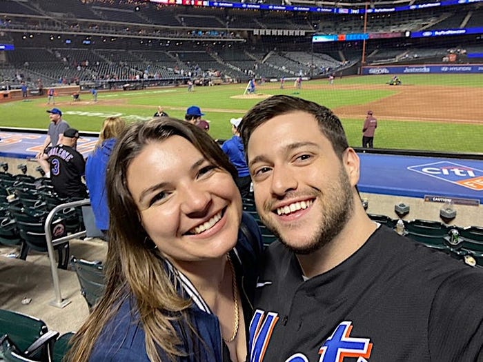 Meredith Wilshere and her boyfriend at a Mets game smiling and looking at the camera.