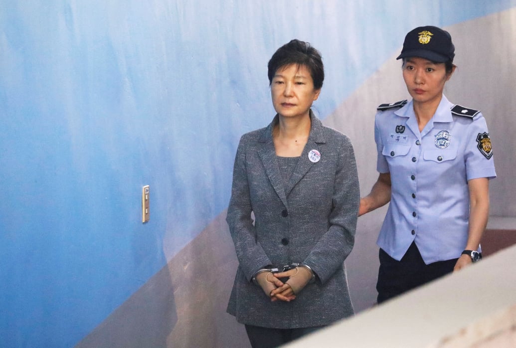 An officer escorts Park Geun-hye, who’s wearing handcuffs, into court.
