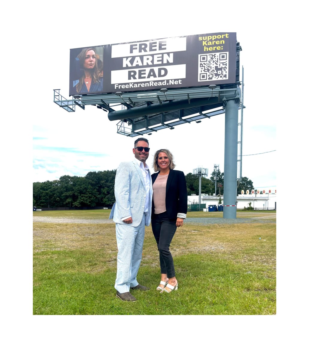 Jon Silva and Leigh pose in front of a Free Karen Read billboard.