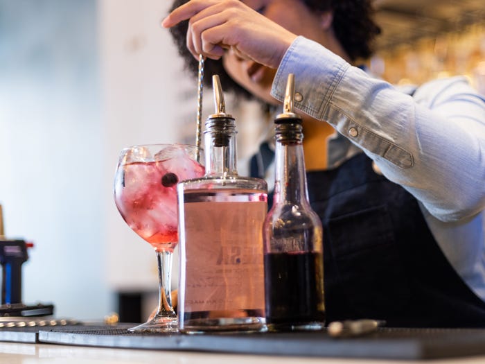 bartender mixing a pink drink in a highball glass at a bar