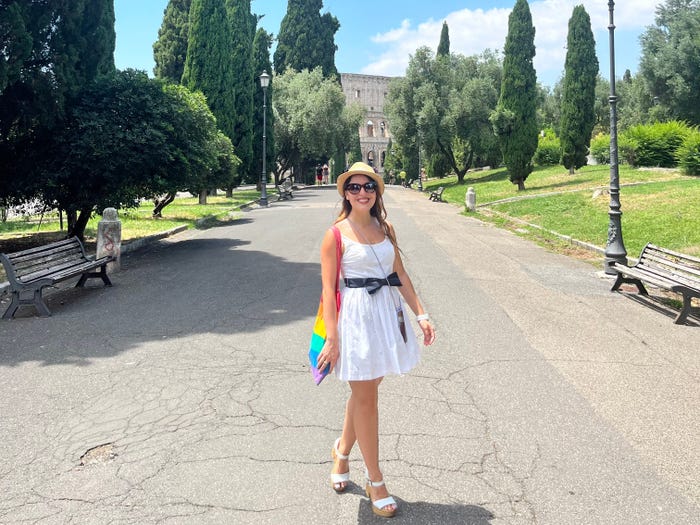 Federica Bocco, a woman wearing a white dress, with the Colosseum and trees in the background