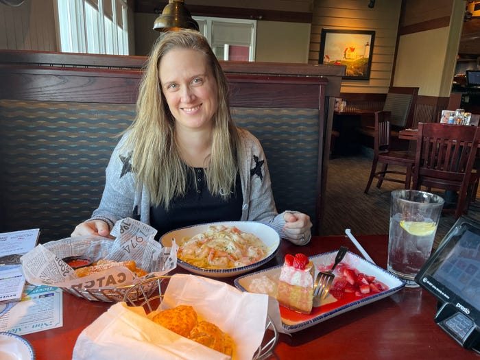 The writer smiles sitting at a table filled with cheddar biscuits, mozzarella sticks, shrimp Alfredo, and strawberry cheesecake at Red Lobster