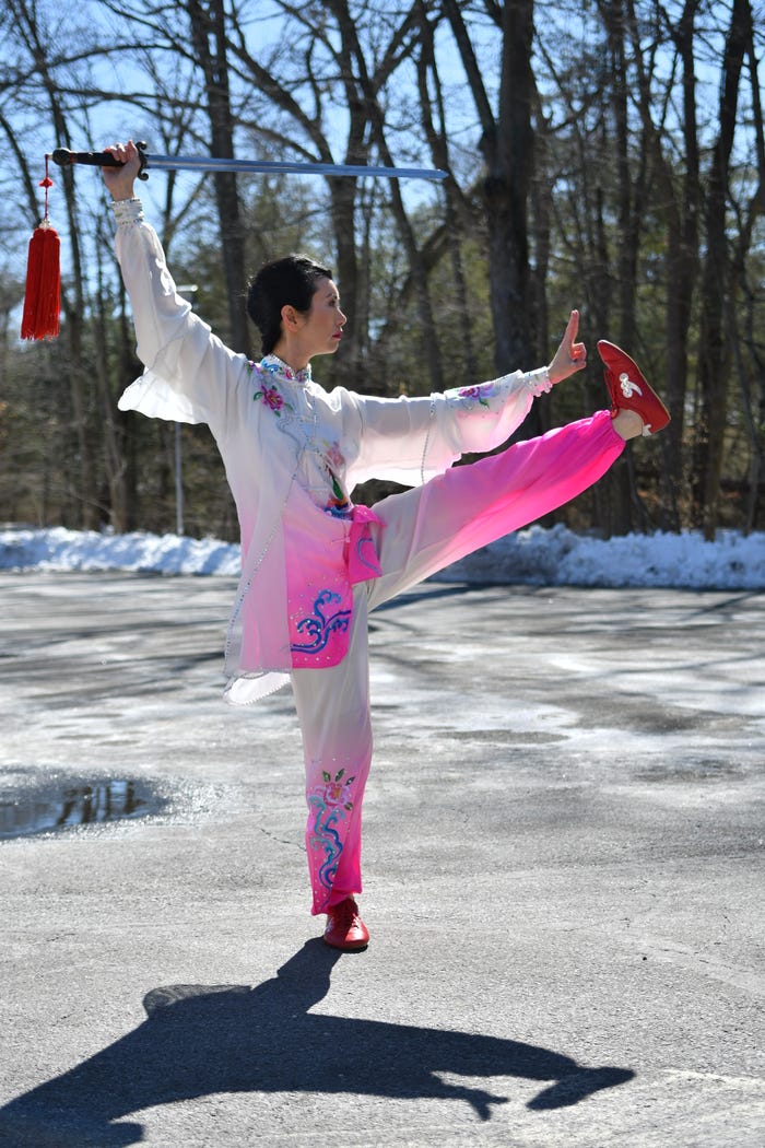 Tai chi instructor Shirley Chock performing sword tai chi in a white and pink uniform outside