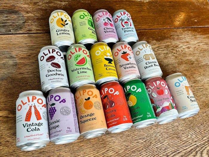 16 cans of Olipop laid out on a wooden table in a pyramid shape.