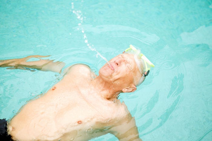A senior man playing in a swimming pool.