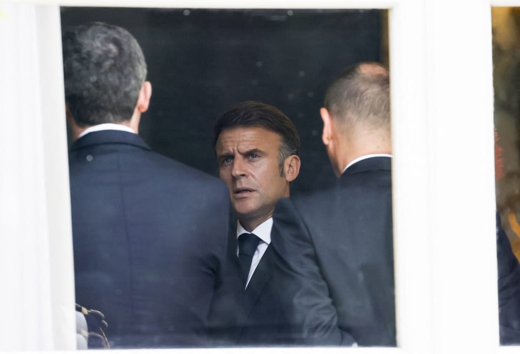 Emmanuel Macron seen through a window speaking to advisors