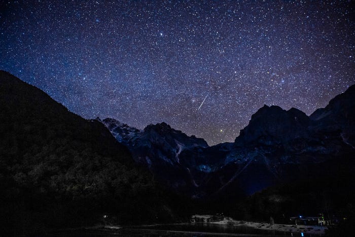 image of night sky full of stars and meteor over mountains