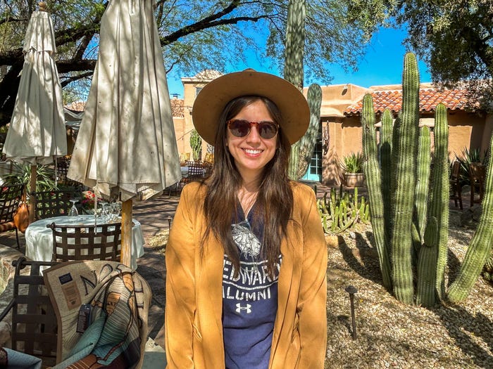 The author in a cowboy hat and sunglasses stands smiling in front of cacti and an adobe building in Scottsdale