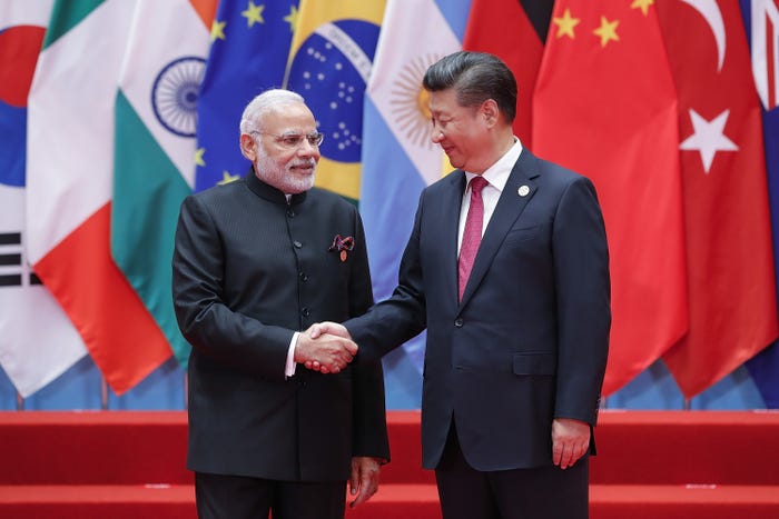 Indian Prime Minister Narendra Modi and Chinese leader Xi Jinping shaking hands against backdrop of G20 flags.