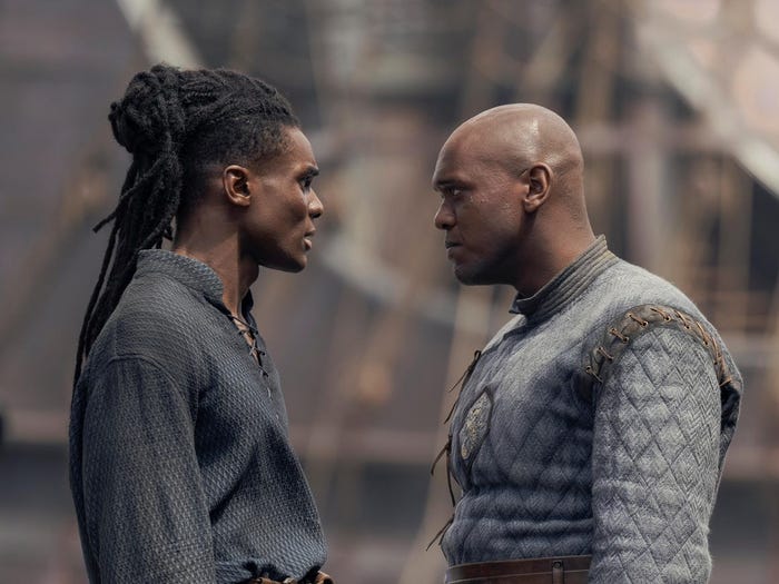 clinton liberty and abubakar salim as addam and alyn of hull, two young men in blue clothing. addam has long hair, arranged in dreadlocks and pulled back, while alyn is bad. they're looking at each other in a shipyard